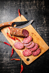 Wall Mural - Pieces of salami sausage on a cutting board with pods of dried chili peppers. 