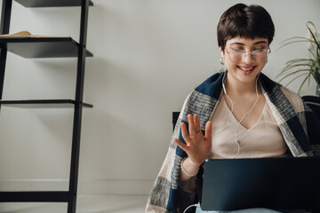 Cheerful short-haired woman making video call via laptop while sitting at home