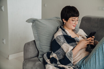 Wall Mural - Young smiling woman using mobile phone while laying on sofa