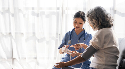 Wall Mural - Happy senior woman having her blood pressure measured in a nursing home by her caregiver. Happy nurse measuring blood pressure of a senior woman in living room