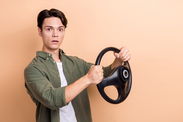 Canvas Print - Photo of young funny student guy wear khaki shirt drive steering wheel simulation new car license scared accident isolated on beige color background