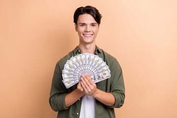 Wall Mural - Portrait of cheerful satisfied man arms hold dollar banknotes bills isolated on beige color background