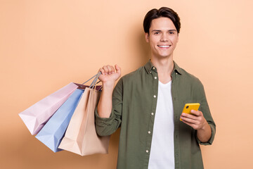 Sticker - Photo of shopaholic guy student handsome person wearing stylish khaki shirt use phone for eshop hold much packages isolated on beige color background