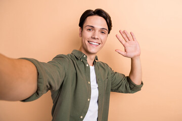 Poster - Photo of optimistic handsome cool guy with brunet hair dressed khaki shirt doing selfie waving palm isolated on beige color background