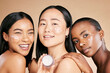 © Jade Maas/peopleimages.com - Beauty, portrait and face cream by diverse women in studio for wellness or grooming on brown background. Friends, skincare and skin lotion for girl group with different, facial and product isolated