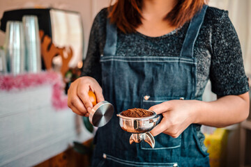 Close-up of hand barista or coffee maker holding portafilter and coffee tamper making an espresso coffee.