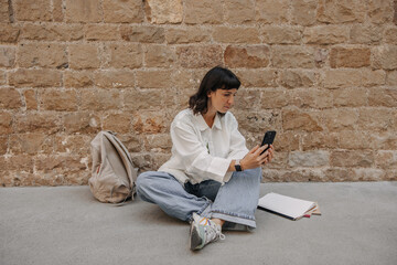 Wall Mural - View of pretty dark-haired woman looking at phone and chatting. European with short hair in hands smartphone outdoors. Use technology concept