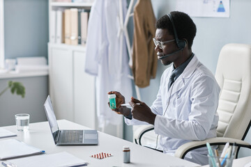 Wall Mural - Young black doctor holding bottle of pills during online consultation