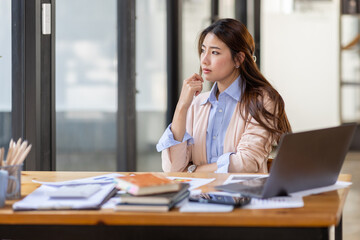 Wall Mural - Image of young beautiful brooding Asian woman working with laptop while sitting at laptop in office, thinking of professional plan, project management, considering new business ideas.