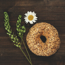 Bun In Form Of Ring Of Whole Grain Flour With Cereals And Seeds. Healthy Food. Homemade Pastries. Dark Wooden Background Decorated With Chamomile Flower And Green Plant. Copy Space. Close-up. 