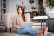 © sepy - Happy woman wearing headphone and using laptop while relaxing at home