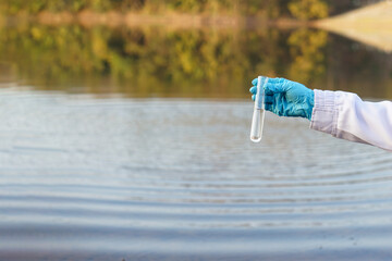 Closeup researcher hands wears blue gloves holds test glass tube that contain sample water from the lake. Concept, explore, inspect quality of water from natural source.         