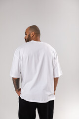 Wall Mural - Back view of a bald african american guy with a beard in a white blank t-shirt. Mock-up.