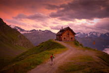 Man Hiking Towards Mountain Hut At Sunset