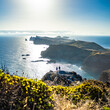 © Michael - Backpacker couple enjoys panoramic view from steep cliff over seascape and along rugged foothills of Madeira coast at sunrise. Ponta do Bode, Madeira Island, Portugal, Europe.