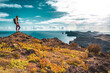 © Michael - Backpacker woman enjoys panoramic view from a steep cliff overlooking the sea and the rugged foothills of Madeira's coast in the morning. Ponta do Bode, Madeira Island, Portugal, Europe.