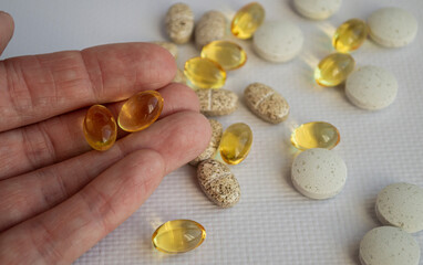 Two capsules of fish oil lie on the fingertips in the palm of the hand, and scattered medicines can be seen nearby.  The concept of a person going to drink vitamins.