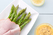 Fresh cooked green asparagus with ham slices, Hollandaise sauce on the side, photographed overhead on light blue wood (Selective Focus, Focus on the top asparagus heads, the ham and the sauce)