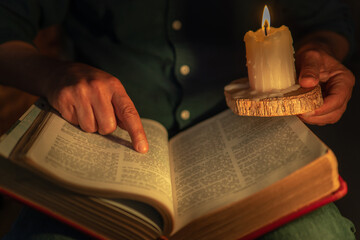 Wall Mural - Unrecognizable man studying the bible pointing with his finger at a biblical passage lighting up with a candle