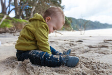 Young Boy Sitting At Waihi Beach In Orokawa Scenic Reserve, New Zealand