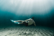 Full Length Of Man Swimming Underwater In The Ocean Close To The Sand