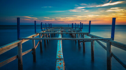 Canvas Print - view of wodden pier on blue sea side with sunset colors and clouds at horizon