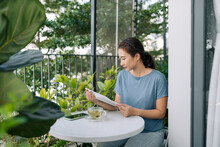 Young Woman Reading A Book On Urban Rooftop Garden.