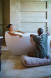 © Jovo Jovanovic/Stocksy - Woman talking to friend relaxing in bathtub at home