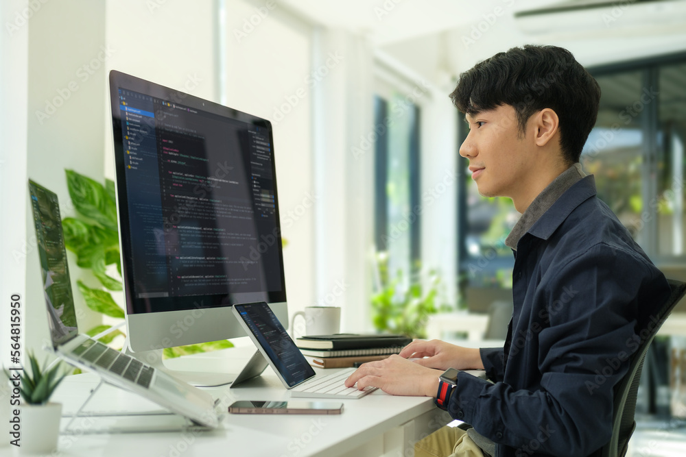 Side view of smart programmer looking at computer monitor and typing data code, developing web project at  workstation.