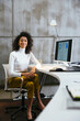 © BONNINSTUDIO/Stocksy - Curly woman wearing casual clothes working on computer in office