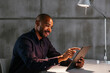 © BONNINSTUDIO/Stocksy - Smiling man using tablet in dark office