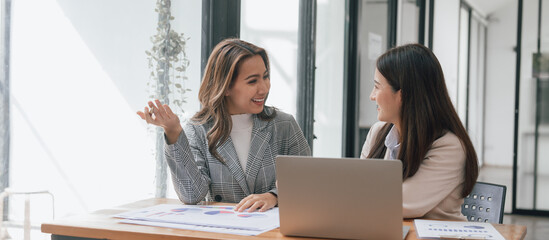 Two young pretty asia business woman in suit talking together in modern office workplace, Thai woman, southeast asian, face to face, talking