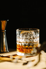 Wall Mural - whisky drink on a wooden table with a barspoon and a jigger on black background