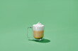 © Marc Tran/Stocksy - Cappuccino in glass cup with double walls isolated on green background