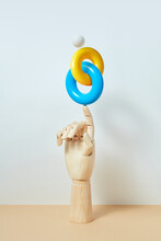 Wooden Hand With Linked Blue And Yellow Rings.