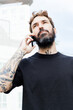 © Berena Alvarez/Stocksy - bearded man with tattoos using his mobile phone
