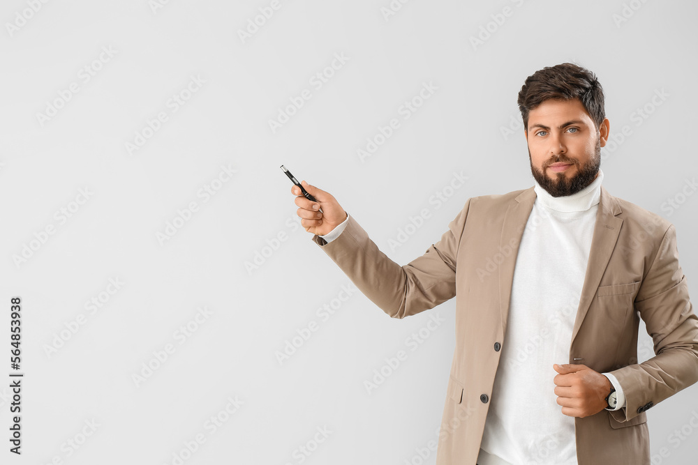 Handsome young businessman with pen on light background