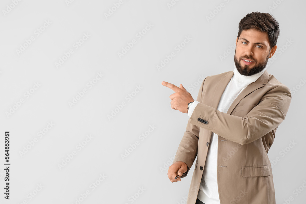 Handsome young businessman in beige jacket pointing at something on light background