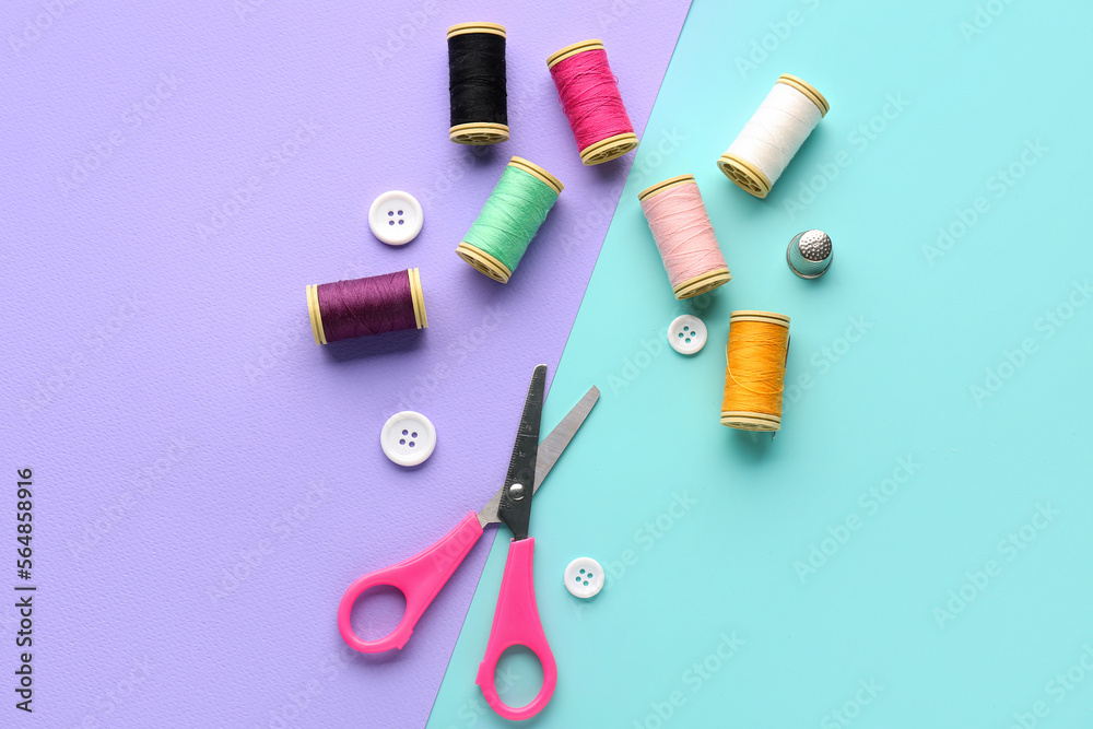 Thread spools, buttons and scissors on color background