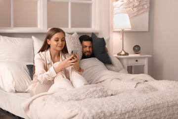 Canvas Print - Young man cannot sleep because of his wife using mobile phone in bedroom