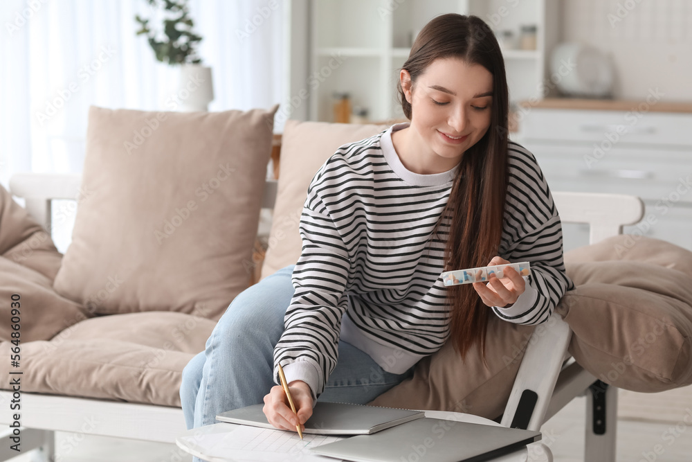 Young woman holding container with vitamin supplements at home