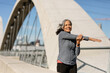 © McKinsey Jordan/Stocksy - Smiling Woman Stretches Arms Before A Morning Run On A Bridge