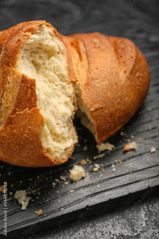 Board with loaf of fresh bread on black background