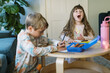 © Serena Burroughs/Stocksy - Happy little girl drawing at a table with her brother sitting nearby