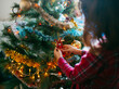 © Jimena Roquero/Stocksy - Kid  hanging ornament in Christmas tree in daylight