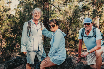 Happy group of senior retirees  hiking in mountain park stops to rest. Elderly man and women enjoying healthy lifestyle in nature looking at camera smiling