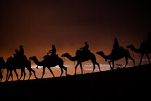 Silhouette Of People Riding Camels In The Desert Dunes