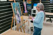 © Jimena Roquero/Stocksy - Grey-haired woman with glasses in art school  analyzing her artwork