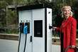 © Malquerida Studio/Stocksy - Woman plugging cable on electric car Charge Station