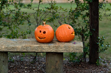 Two Carved Pumpkins On A Bench Outside